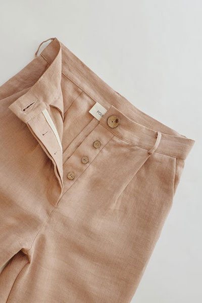 Close-up of a linen trouser waistband with a buttoned fly and topstitched pocket.