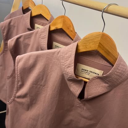 Identical tops on hangers, each with a woven brand label, made as one run in the studio.