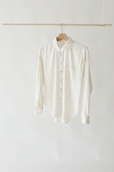 A cream linen shirt on a wooden hanger against a white wall.