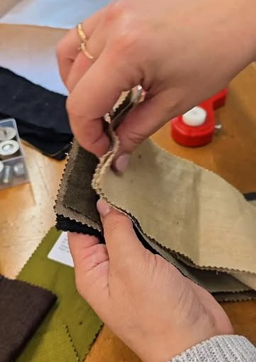 Hands leafing through fabric swatch books on the studio bench.