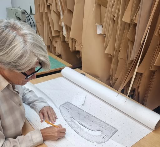 Olga drafting a pattern by hand at the cutting table, with finished card patterns hanging behind.