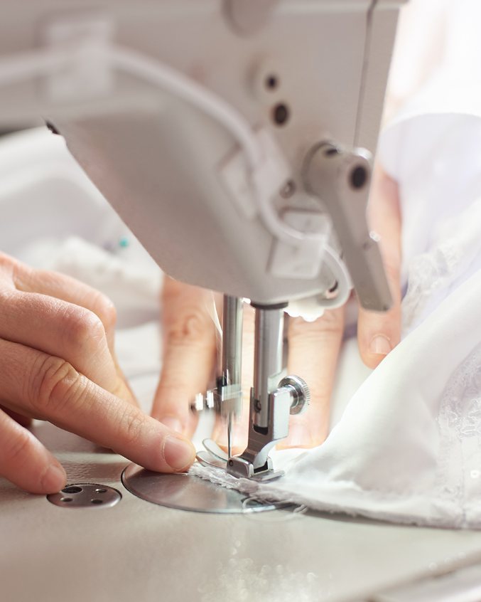 Hands guiding white fabric through a sewing machine.
