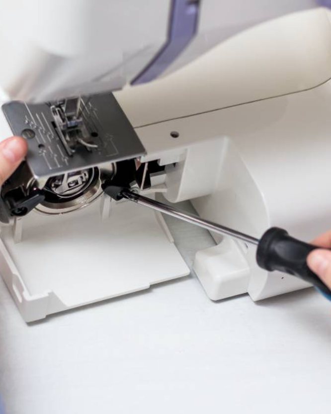 A sewing machine being serviced, with the needle plate lifted to reach the bobbin area.