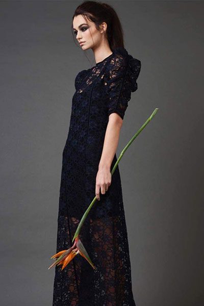 A long black lace dress worn by a model holding a single stem.