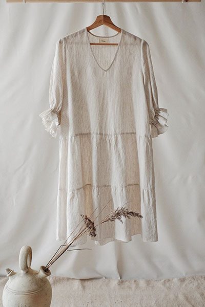 A cream linen dress with a gathered tier hanging on a wooden rail.